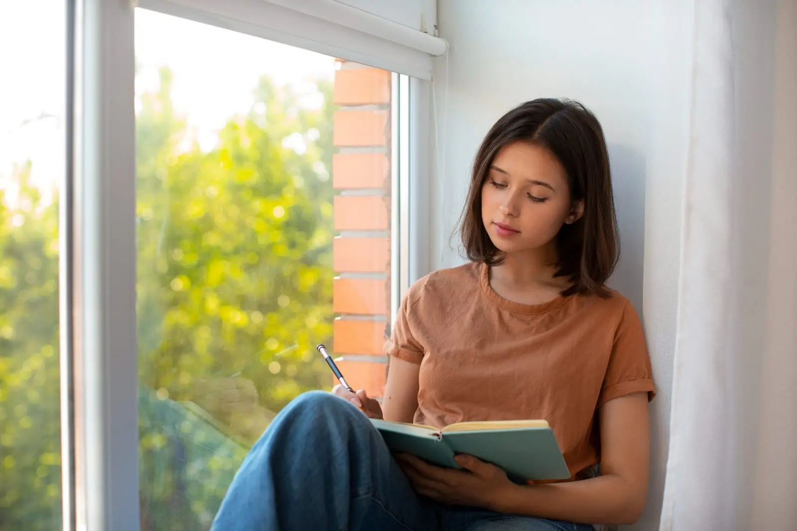 Estudante olhando o celular durante uma pausa nos estudos, com livros abertos na mesa
